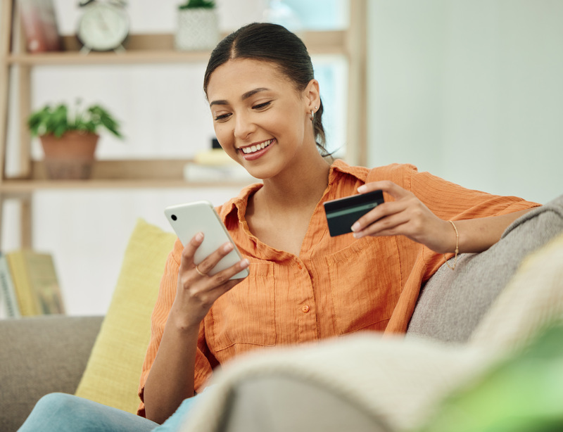 Mujer sonriente con tarjeta y celular en mano solicitando un crédito de bajo monto